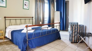 A neatly made bed with a metal frame and blue bedding, a chair with striped upholstery, and a wall-mounted TV. - Studio in the city center with private parking (AREZZO)