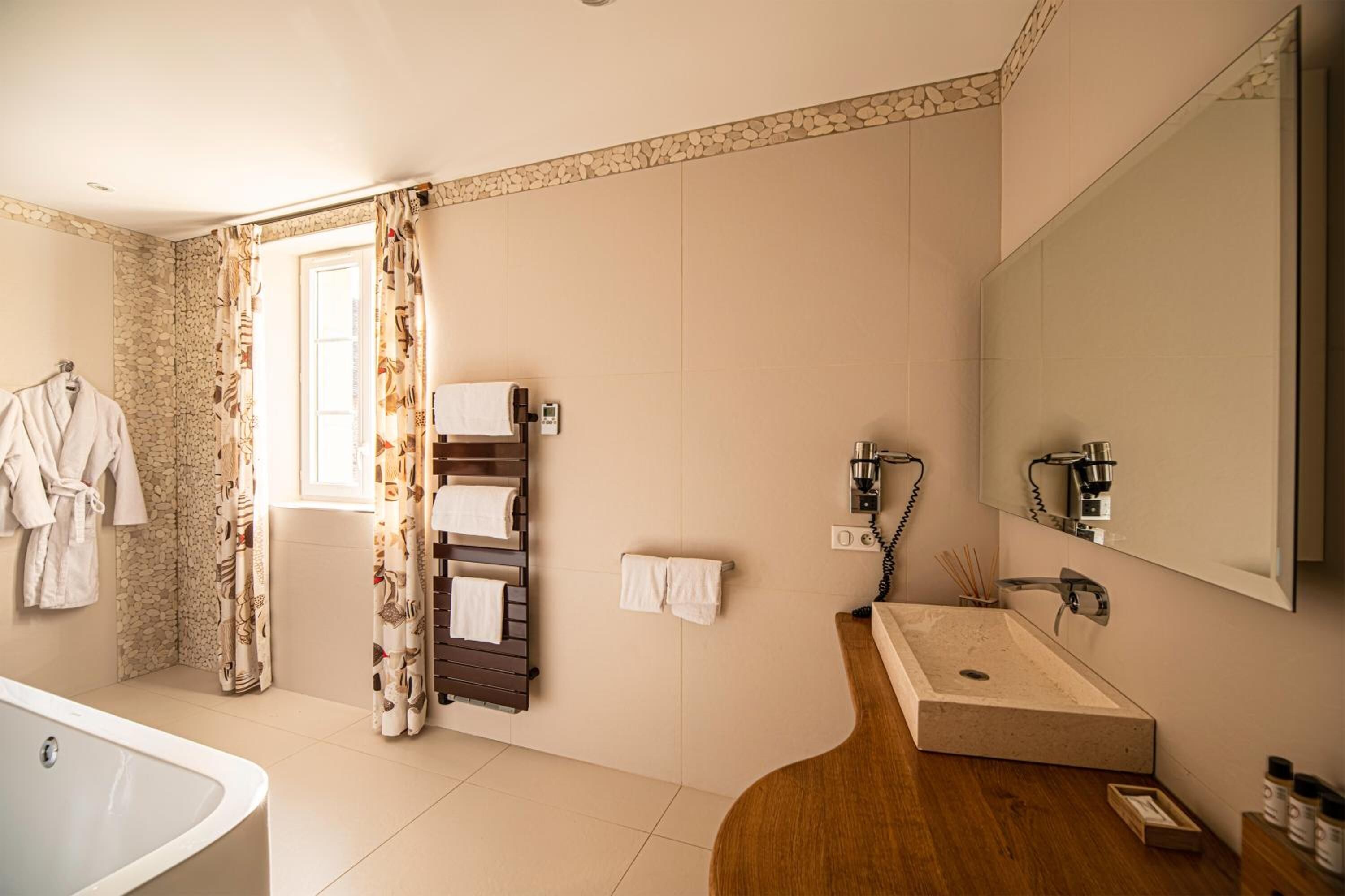 A modern bathroom with a bathtub, a wooden vanity with a sink, and a large mirror. There are towels hanging on a rack and a shower curtain with a floral pattern.