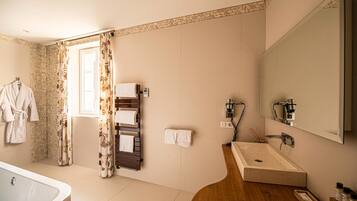 Un baño moderno con bañera, tocador de madera con lavamanos y un espejo grande. Hay toallas colgadas en un perchero y una cortina de ducha con estampado floral.