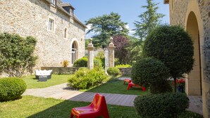A stone building with a courtyard, a wooden deck, and red chairs. - Château de la Falque, The Originals Relais  (Saint-Geniez-d'Olt-et-d'Aubrac)