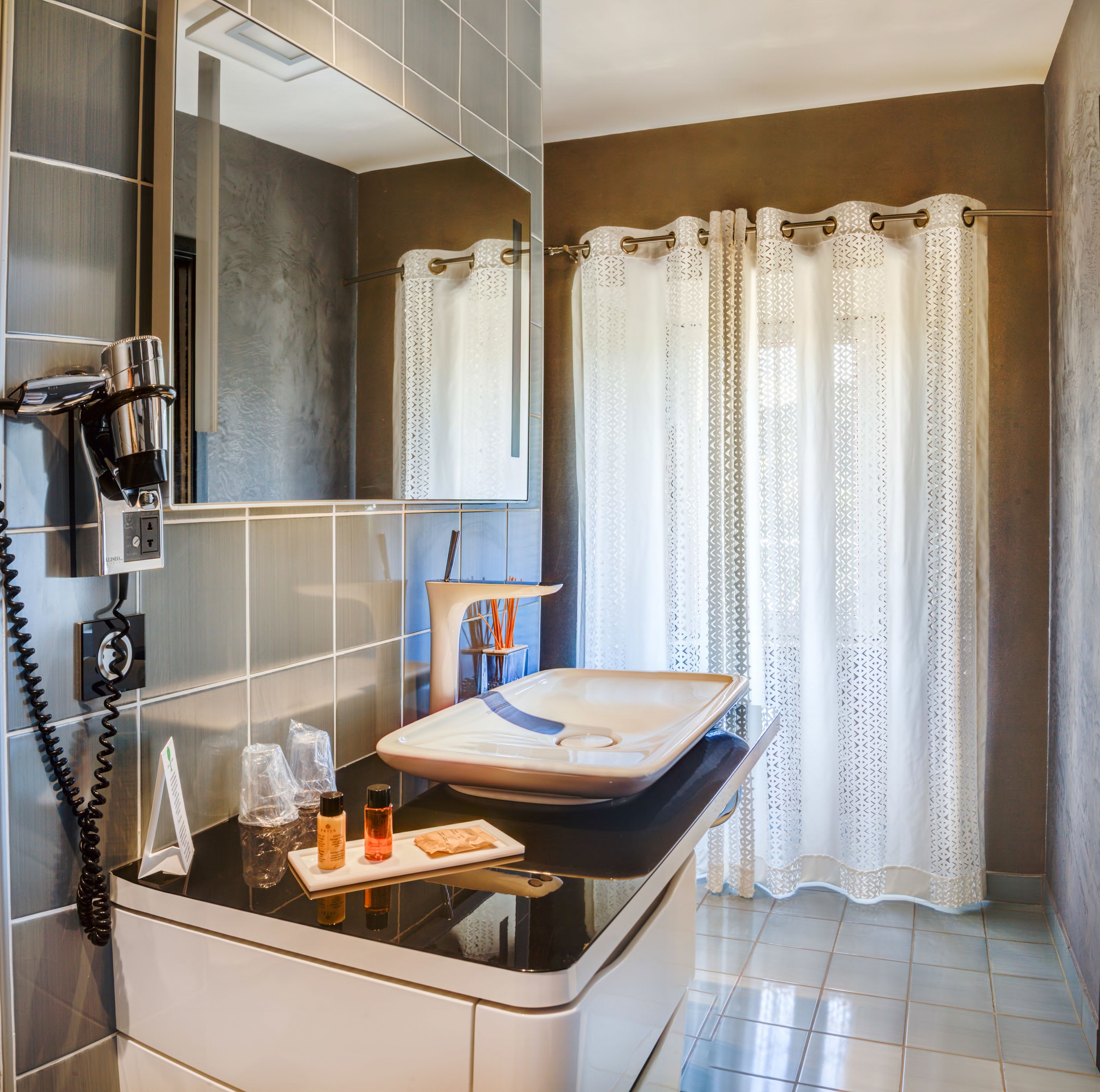 A bathroom with a modern sink, a mirror, a hairdryer, and a shower curtain.