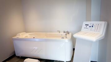 A modern bathroom with a large white bathtub, a small step stool, and a digital control panel.