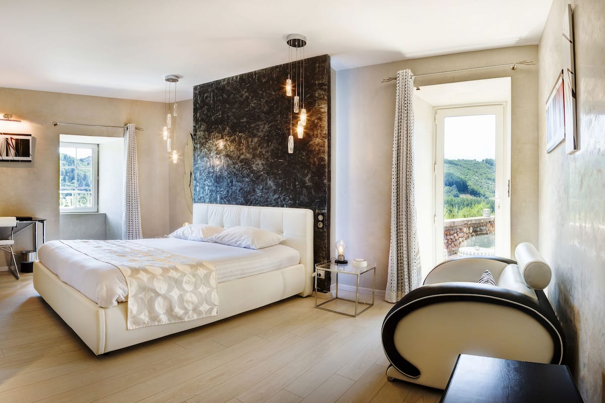 A modern bedroom with a large bed, bedside tables, a desk, and a view of the outdoors.
