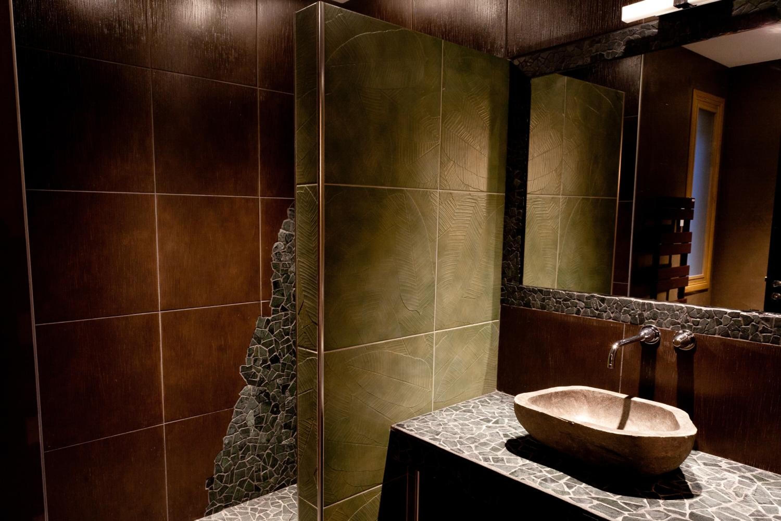 Un baño con lavamanos de piedra, paredes de madera oscura y un espejo.