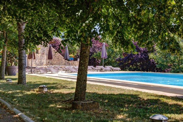 A poolside area with lounge chairs, umbrellas, and a stone building in the background. - Château de la Falque, The Originals Relais (Saint-Geniez-d'Olt-et-d'Aubrac)