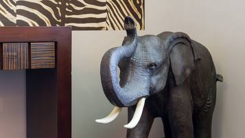 Una escultura de madera de un elefante con colmillos, situada frente a un fondo con estampado de cebra.