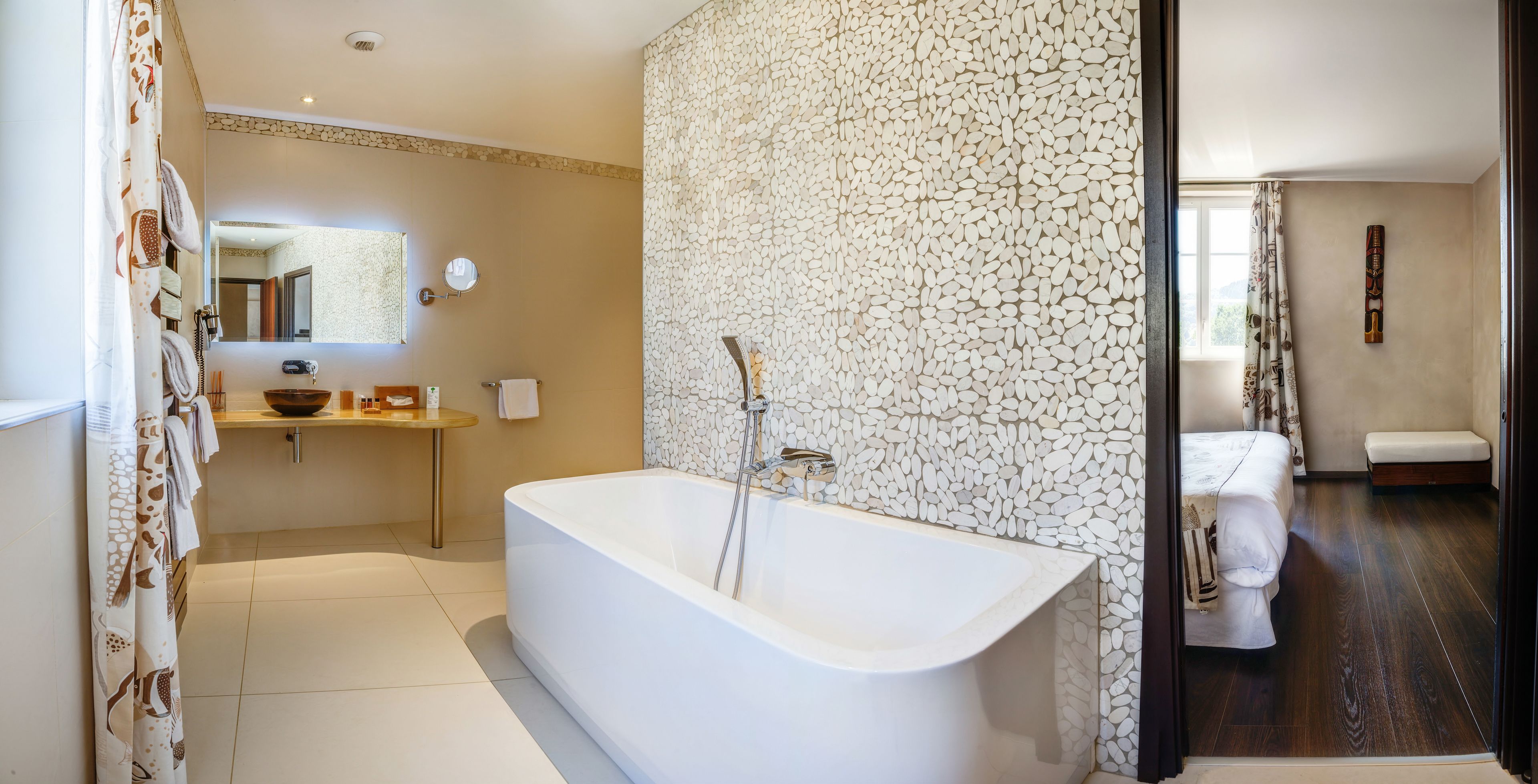 A modern bathroom with a freestanding bathtub, a round mirror, a vanity with a bowl sink, and a stone-patterned wall.