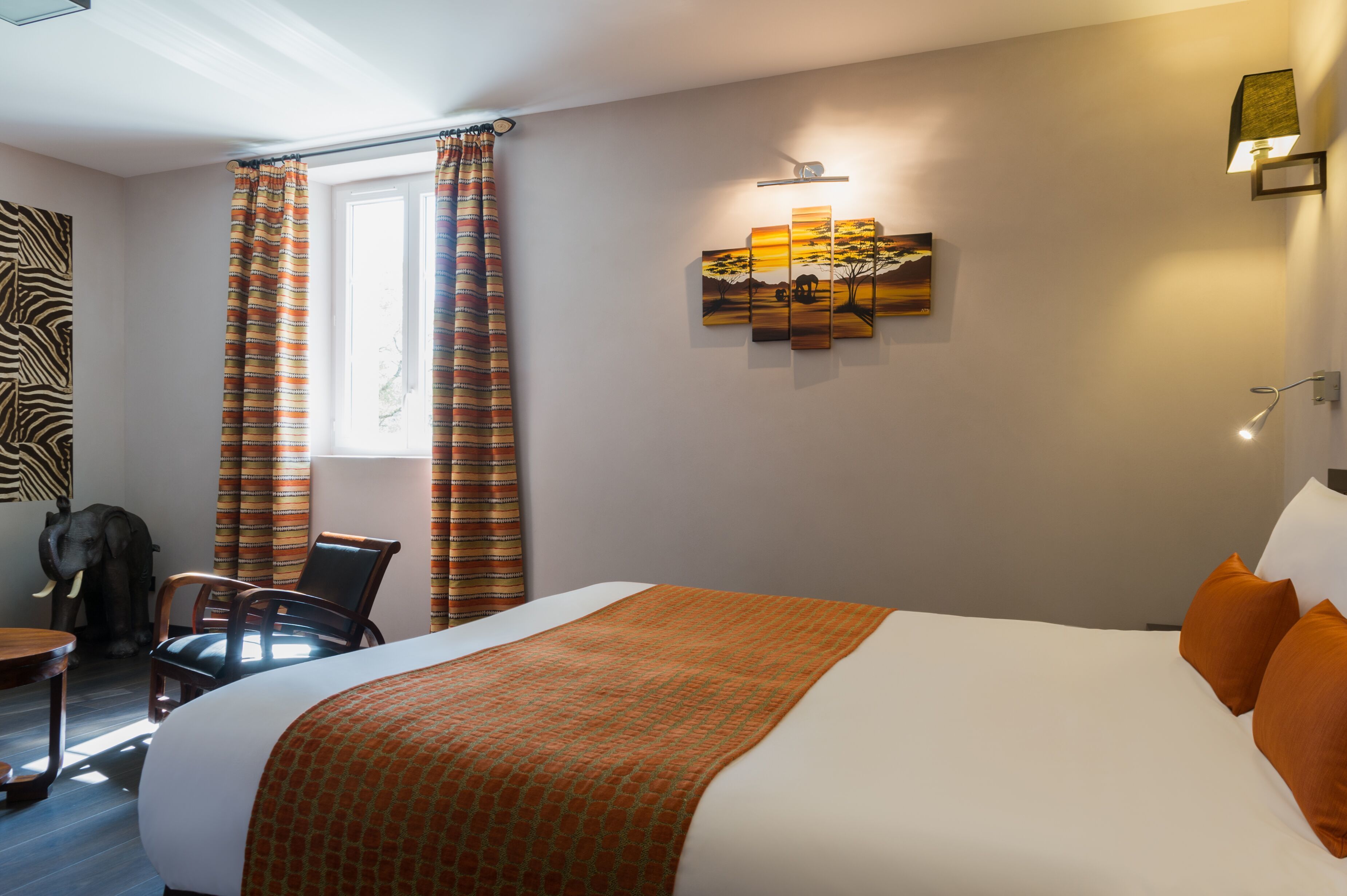 A hotel room with a large bed, a chair, a desk, and a zebra-patterned wall art.