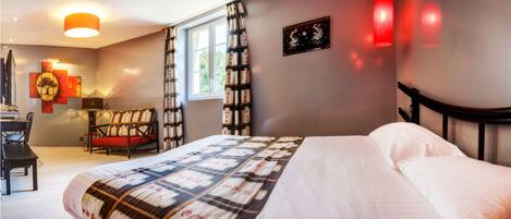 A bedroom with a bed, a desk, a chair, a window, and artwork on the walls.