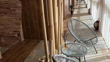 Een gang met bamboezuilen, rieten stoelen en een betegelde vloer.