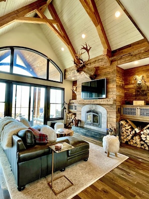 A spacious living room with a fireplace, leather sofa, and a large TV.