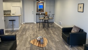 Un salon moderne avec une table basse en bois, un canapé noir et un coin repas avec une cuisine en arrière-plan.