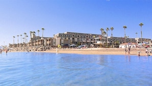 Un hôtel en bord de mer doté de nombreux balcons, d’une plage de sable et de palmiers.