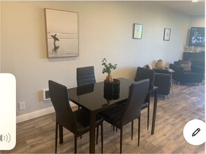 A dining area with a black table and chairs, a potted plant, and a painting on the wall.