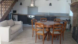 A dining area with a round table and chairs, a sofa, a washing machine, and a staircase. - STONE HOUSE RENOVATED WITH TASTE WITH TENNIS IN A HAVEN OF PEACE (Féniers)