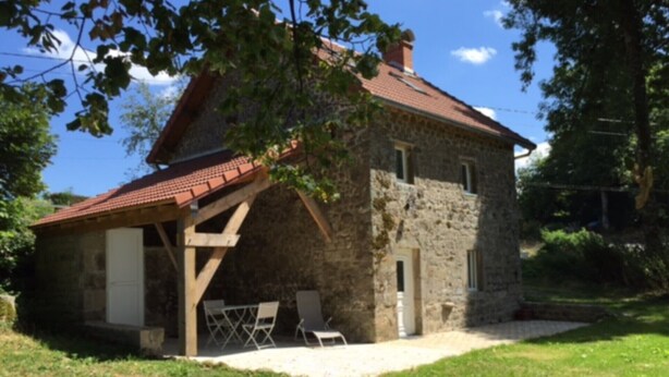 A stone house with a tiled roof, a wooden porch, and a small patio area with chairs. - STONE HOUSE RENOVATED WITH TASTE WITH TENNIS IN A HAVEN OF PEACE (Féniers)