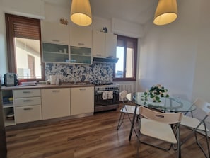 A compact kitchen with wooden flooring, white cabinets, a gas stove, and a glass dining table with chairs.