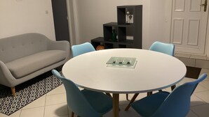 Un comedor con una mesa redonda blanca, cuatro sillas azules, un sofá gris y una alfombra estampada.