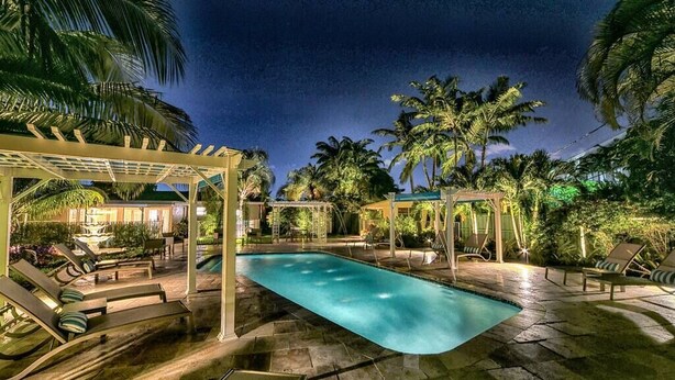 Un área de piscina nocturna con sillones de descanso y una pérgola.