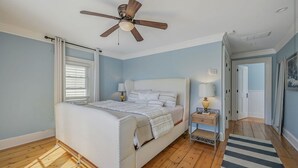 Een slaapkamer met een bed, een plafondventilator, een nachtkastje met een lamp en een raam met jaloezieën.