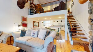 Un vaste espace de vie doté d’un haut plafond, d’un escalier en bois et d’une cuisine située au fond de la pièce.