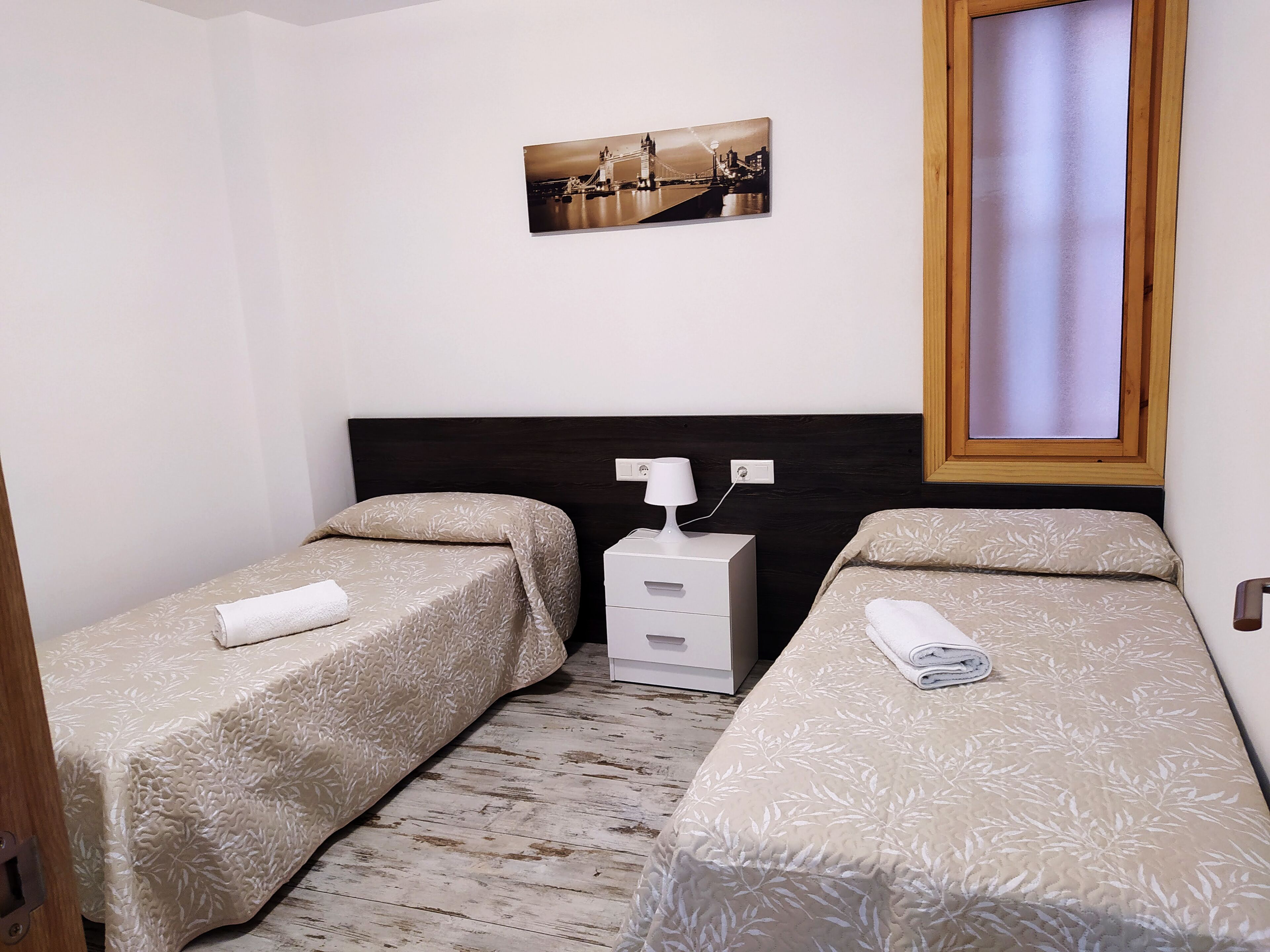 Ein Hotelzimmer mit zwei Betten, einem Nachttisch, einer Lampe, einem Gemälde und einem Fenster.