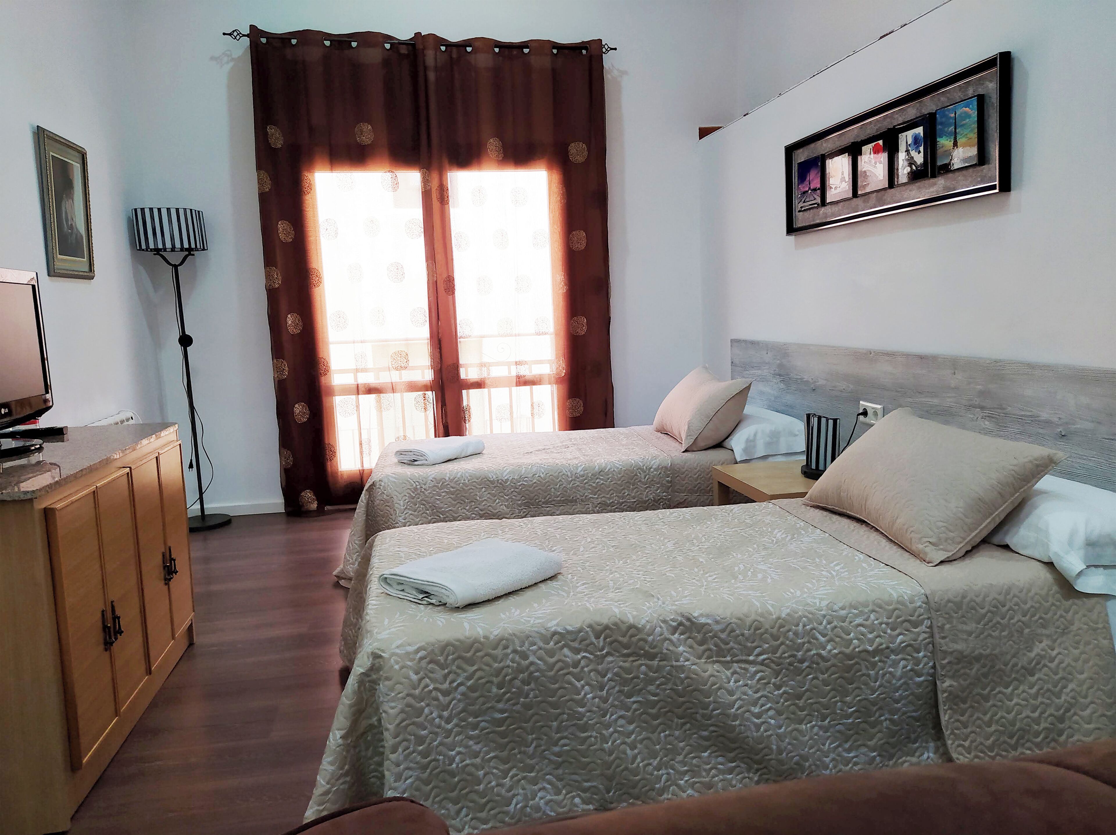 Una camera d'albergo con due letti, una scrivania, una lampada e un quadro appeso al muro.