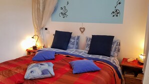 Een net opgemaakt bed met een rood-oranje geruit beddegoed, blauw-witte kussens en een decoratieve wandhanger.