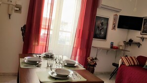 Een eetgedeelte met een tafel voor vier personen, een bank en een aan de muur bevestigde televisie.