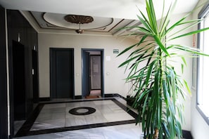 Un hall d’hôtel avec un sol en marbre, une grande plante en pot et un ventilateur de plafond.