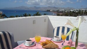 A table with breakfast items, a vase with flowers, and a view of the sea and mountains. - Apartment the Quintero (Tías)