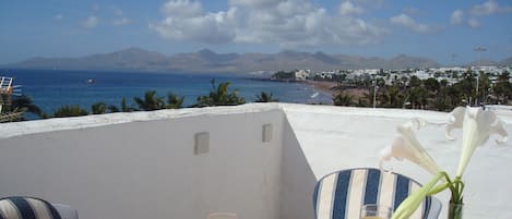 Una mesa con alimentos para el desayuno, un florero con flores y vista al mar y a las montañas.