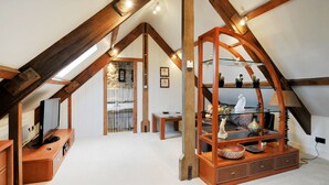 A loft-style room with exposed wooden beams, a glass shelving unit, and a cozy seating area.