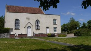 A two-story building with a red-tiled roof, a white door, and two windows on the ground floor.