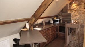 A kitchen with a stone wall, wooden beams, a stainless steel sink, a microwave, and a stove.