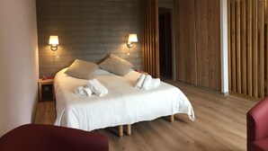 A modern hotel room with a wooden headboard, two bedside lamps, a neatly made bed with white linens, and a red chair. - Village Vacances le Tarbesou - Appartments (Ax-les-Thermes)