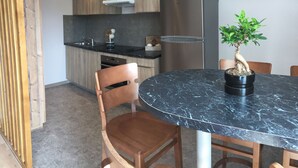 A modern kitchen with a built-in oven, a stainless steel refrigerator, and a potted plant on the dining table. - Village Vacances le Tarbesou - Appartments (Ax-les-Thermes)