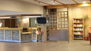 A reception area with a wooden reception desk, a television, a bookshelf, and a potted plant. - Village Vacances le Tarbesou - Appartments (Ax-les-Thermes)