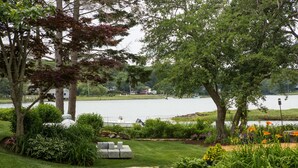 A lakeside garden with a grassy lawn, a stone bench, and a variety of plants. - Spectacular quiet location with partial view of Paddy Creek iKennebunkport! (Kennebunkport)