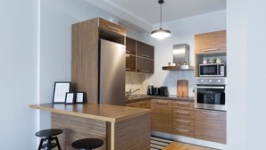 A modern kitchen with wooden cabinetry, a built-in island, bar stools, and stainless steel appliances. - UPSTREET Stylish & Spacious 2BD Apt-Thiseio (Athens)