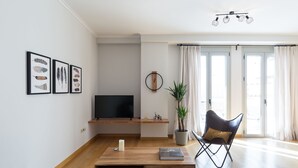 A modern living room with a wooden coffee table, a TV on a stand, a potted plant, and a chair. - UPSTREET Stylish & Spacious 2BD Apt-Thiseio (Athens)