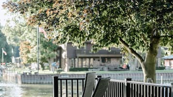 Une terrasse au bord de l’eau avec une table ronde et deux chaises longues.