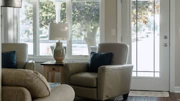 Un salon avec deux fauteuils beiges, une petite table d’appoint avec une lampe, et une vue sur l’extérieur grâce à une grande fenêtre.