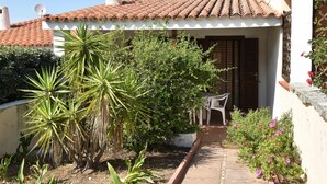 Un petit pati amb teulada, una paret blanca i una porta que dona a una zona exterior coberta.