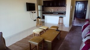 A living room with a sofa, a coffee table, and a kitchen area with a counter and stools. - Ocean Atlantic Residence 1512 (Asilah)