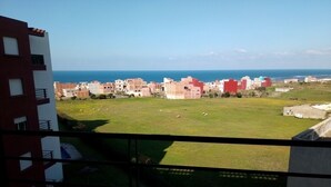 A view from a balcony overlooking a grassy area with buildings in the background and a body of water. - Ocean Atlantic Residence 1512 (Asilah)