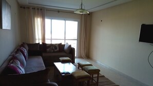 A living room with a sofa, ottomans, a coffee table, and a TV. - Ocean Atlantic Residence 1512 (Asilah)