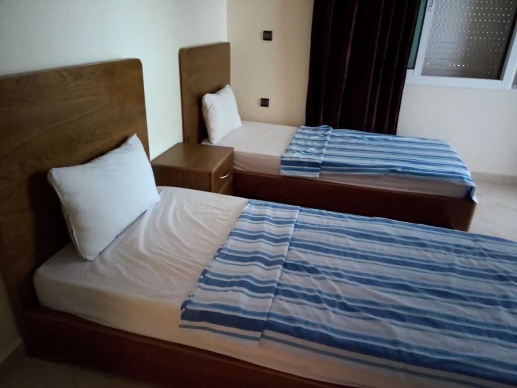 A hotel room with two beds, each with a wooden headboard, a nightstand, and a window with curtains.