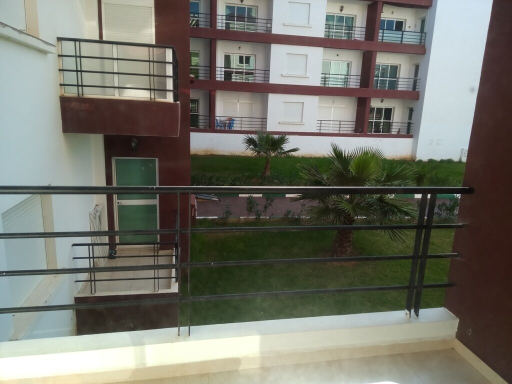 A multi-story residential building with balconies, a green lawn, and a palm tree.