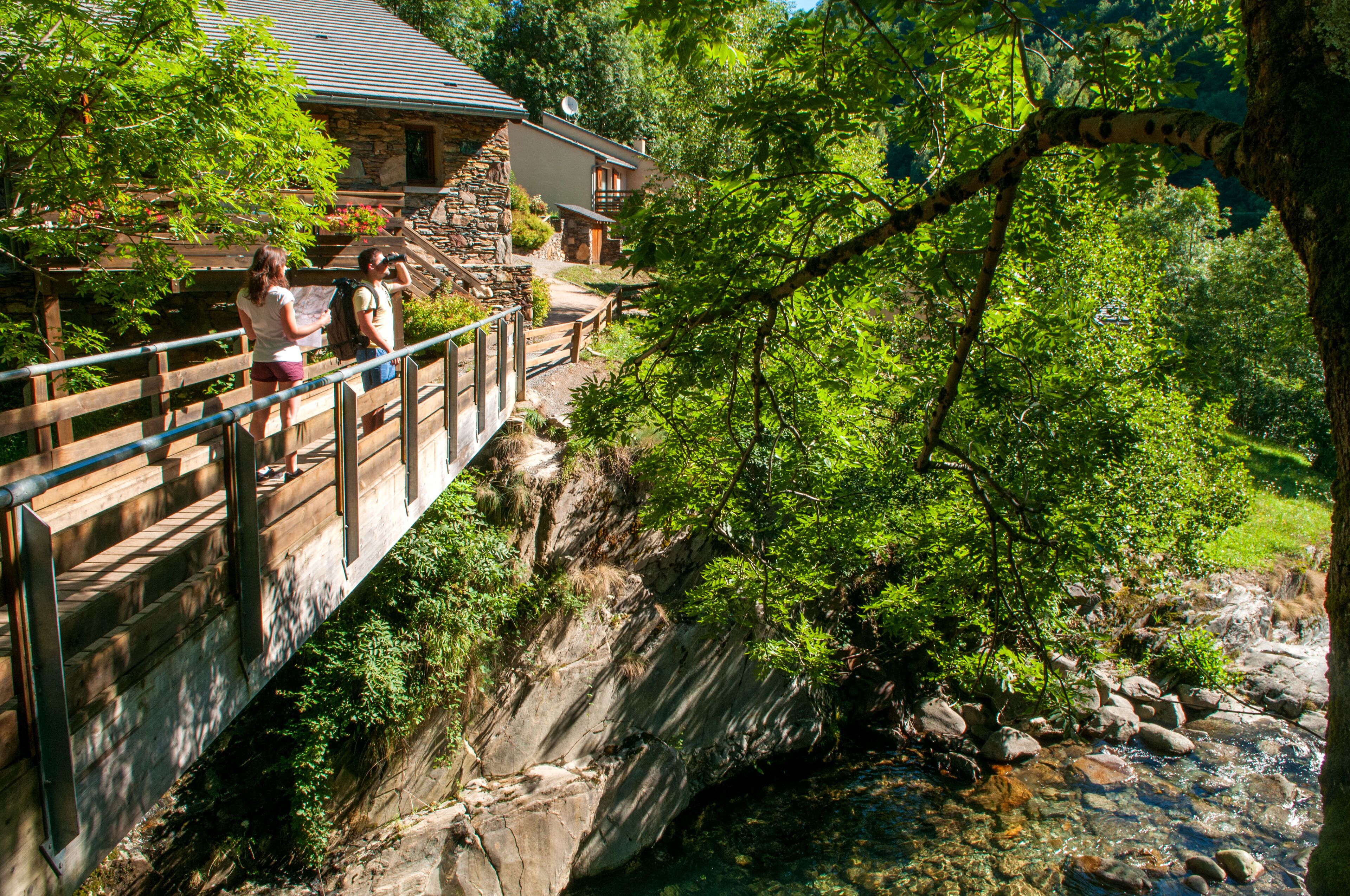 A stone building with a wooden deck overlooking a rocky stream.